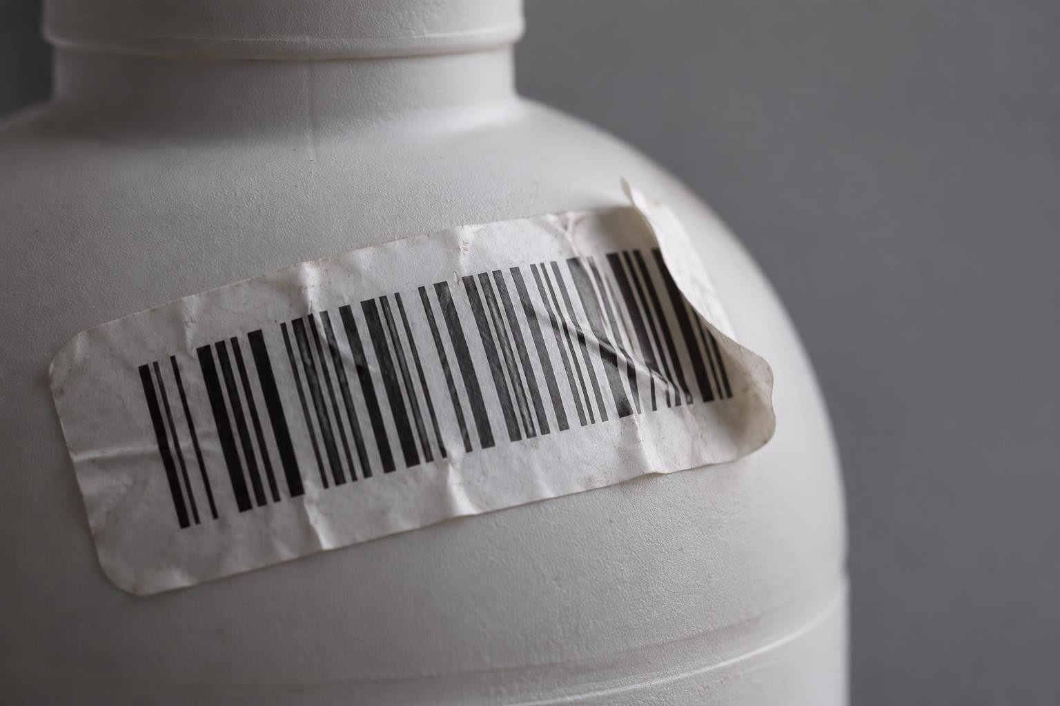 Un'etichetta con codice a barre sgualcita si stacca dalla spalla curva di una bottiglia di plastica